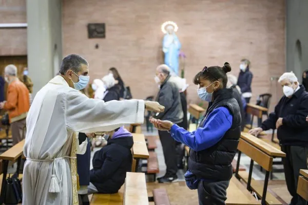 Sacerdote mentre dà la comunione in mano a un fedele / CEI