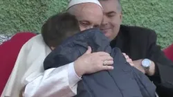 Papa Francesco abbraccia il piccolo Emanuele, nell'incontro con i bambini alla parrocchia di San Paolo della Croce. Sullo sfondo, il parroco Don Roberto Cassano, San Paolo della Croce, Roma, 15 aprile 2018 / Vatican Media - Youtube