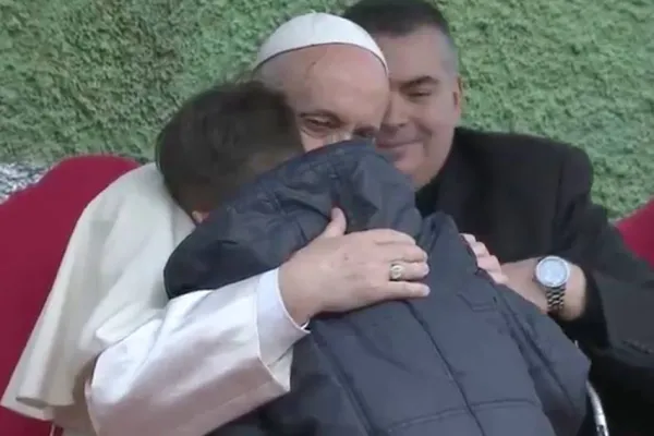 Papa Francesco abbraccia il piccolo Emanuele, nell'incontro con i bambini alla parrocchia di San Paolo della Croce. Sullo sfondo, il parroco Don Roberto Cassano, San Paolo della Croce, Roma, 15 aprile 2018 / Vatican Media - Youtube